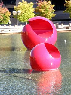 two pink chairs sitting on top of a body of water next to each other in front of a building