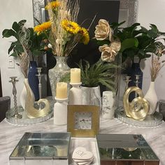 a table topped with lots of vases filled with flowers and other decorative items in front of a mirror