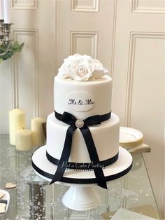 a three tiered wedding cake with black ribbon and white flowers on top, sitting on a glass table