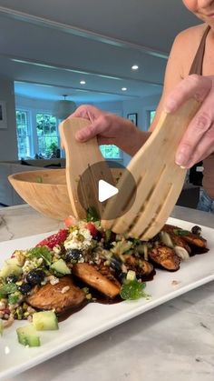 a woman cutting up food on top of a white plate with wooden utensils