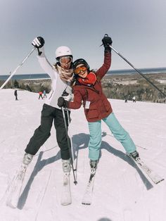 two people on skis posing for a photo in the snow with their arms up