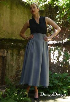 a woman is standing in front of some bushes and trees wearing a black top and grey skirt