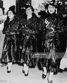 three women in long dresses and hats are walking down the street with their mouths open