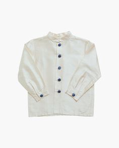 Boy's occasion shirt, crafted from soft and elegant ivory silk, features a stylish smoking collar and fastens at the front with buttons covered in blue silk. Pair with matching silk shorts and a cummerbund for a smart traditional heritage style. Please allow 4 weeks between order and delivery for this bespoke piece to be made Classic Cream Shirt With Buttons, Cream Cotton Top For Formal Occasions, Formal Cream Cotton Top, Cream Collared Shirt With Button Cuffs, Formal Cream Shirt With Button Closure, Beige Buttoned Shirt For Daywear, Beige Shirt With Button Cuffs For Daywear, Formal Beige Tops With Button Cuffs, Formal Cream Shirt With Button Cuffs