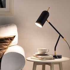 a table with a lamp on it next to a white chair and coffee cup in the corner