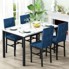 a dining room table with blue chairs and a white marble top in front of a fireplace