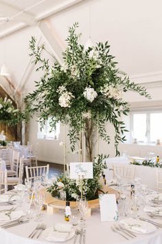 an elegant centerpiece with greenery and white flowers hangs from the ceiling at this wedding reception