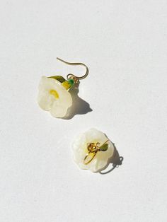 two white flower shaped earrings sitting on top of a white surface with gold ear wires