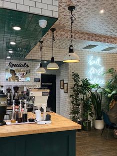 the inside of a coffee shop with lights hanging from the ceiling and plants on the counter