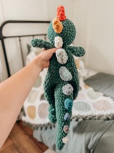 a hand holding a crocheted stuffed animal in front of a bed with pillows