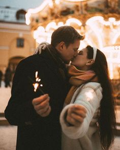 a man and woman standing next to each other holding sparklers in front of a carousel