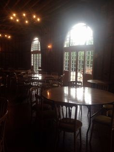 an empty table and chairs in a dark room with large arched windows on the wall