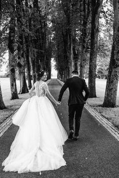 a bride and groom walking down the road holding hands in black and white photo with trees behind them