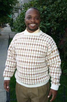 a man standing in front of a fence wearing a sweater