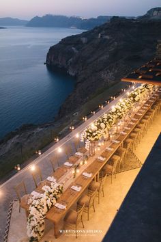 a long table set up with flowers and candles for an outdoor dinner by the ocean