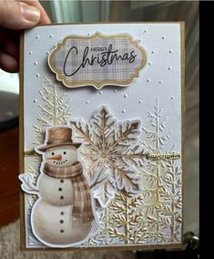 someone is holding up a christmas card with a snowman in the middle and gold trimmings