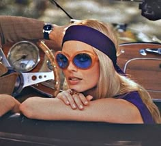 a woman in sunglasses and headband leaning on the steering wheel of an old car