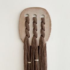 three tassels hanging from a wall on a wooden spoon with metal clips attached to it