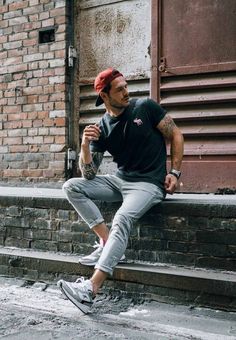 a man sitting on some steps with his foot up and wearing a red hat, black shirt and grey pants