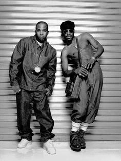 two men standing next to each other in front of a garage door with one holding a purse