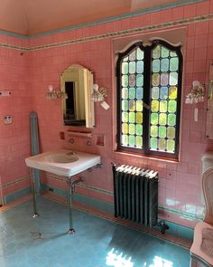 a bathroom with pink walls and blue flooring has a sink, radiator, and window