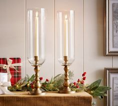 two candles sitting on top of a wooden table next to a christmas wreath and presents