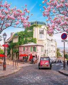 a car is driving down the street in front of some pink buildings and trees with flowers on them