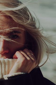 a woman with blonde hair is holding her hand to her face and looking at the camera