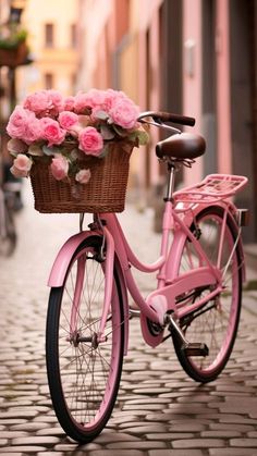 a pink bicycle with flowers in the basket parked on a cobblestone street next to buildings