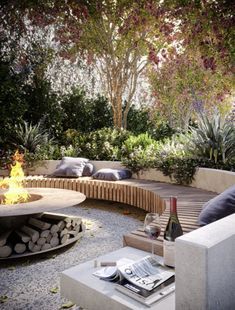 an outdoor fire pit surrounded by trees and seating area with pillows on the couches