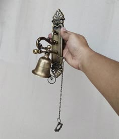 a hand is holding a bell that has been chained to the side of a wall