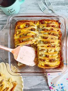 a casserole dish with meat and cheese in it next to a cup of coffee