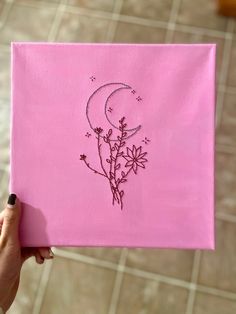 a person holding up a pink piece of cloth with flowers on it and the moon in the background