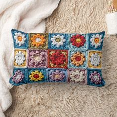 a crocheted pillow with flowers on it sitting on a white rug next to a blanket