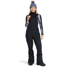 a woman in black snowsuit and hat standing with her hands on her hip while wearing skis