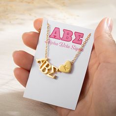 a hand holding a gold necklace with two hearts and the word abe on it