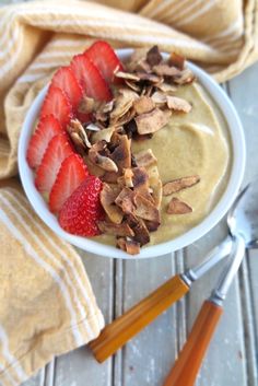 a bowl of food with strawberries and nuts on it next to utensils