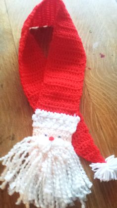 a crocheted santa claus hat and scarf on a wooden table with white pom - poms