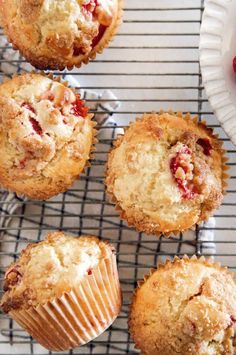 several muffins on a cooling rack next to a plate with strawberries in it