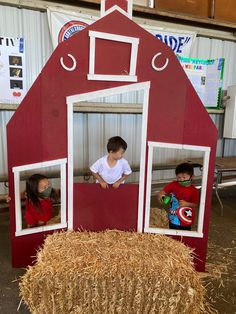 two children standing in front of a red barn with hay bales on the ground