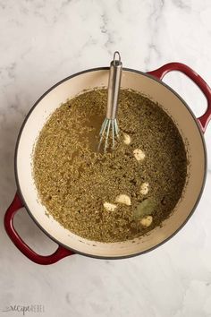 a pot filled with spices on top of a white counter next to a whisk