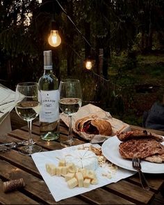 an outdoor table with wine, cheese and bread on it next to two glasses of wine