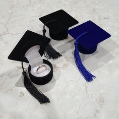 a graduation cap, ring box and tassel on a marble surface