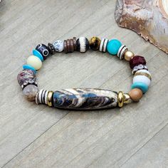 This bracelet is composed with an array of different beads. The main focal bead is a Tibetan hand painted stone bead in browns, cream, a hint of turquoise and red. It complements the other assorted gemstones and bone beads in this bracelet, One of a kind! Assorted gemstones Assorted ethically sourced bone beads Assorted glass beads Assortment of wood, shell, and brass with rhinestones Strong stretch cord Fits a wrist up to 6.75" Created in studio - Wilmington, NC Diy Bracelet Designs, Painted Stone, Hand Painted Stones, Natural Stone Bracelets, Bone Beads, Wilmington Nc, Bead Bracelets, Diy Bracelet, Focal Bead