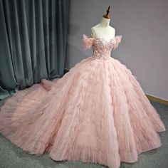 a pink ball gown is displayed on a mannequin stand in front of curtains