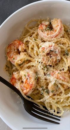 a white bowl filled with pasta and shrimp on top of a table next to a fork