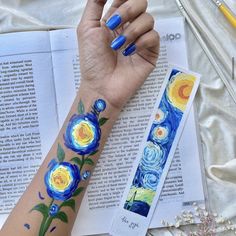 a woman's arm with blue and yellow flowers on it, next to an open book