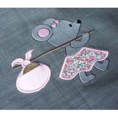 an embroidered teddy bear holding a flower on top of a blue shirt with pink accents