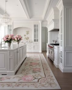 a large kitchen with white cabinets and pink flowers on the countertop, along with an area rug