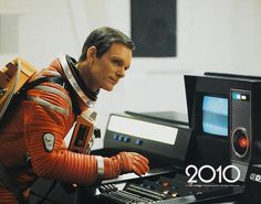 a man in an orange space suit sitting at a desk with a computer and sound equipment